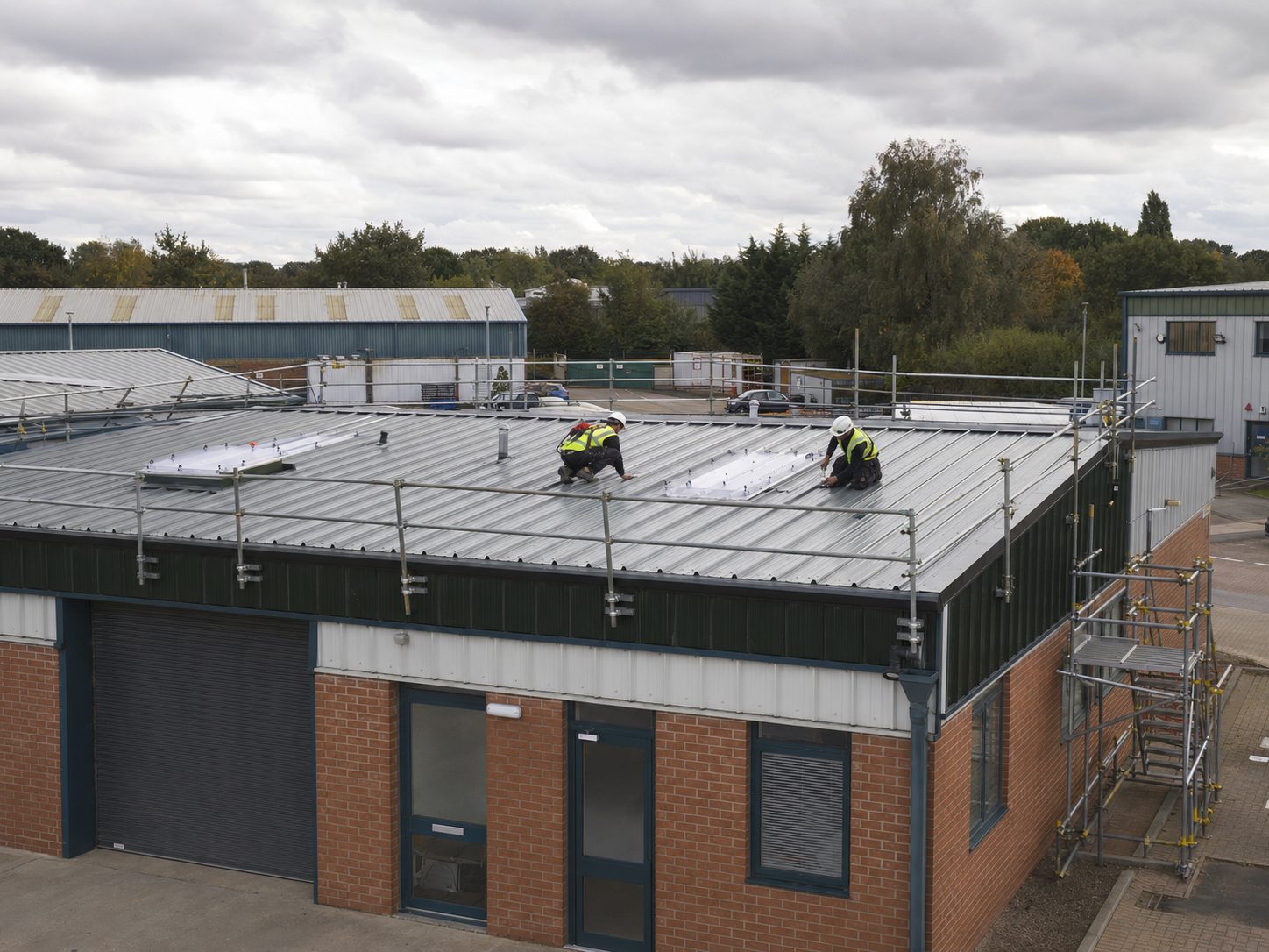 Roofers working on a metal profile commercial roof with edge protection